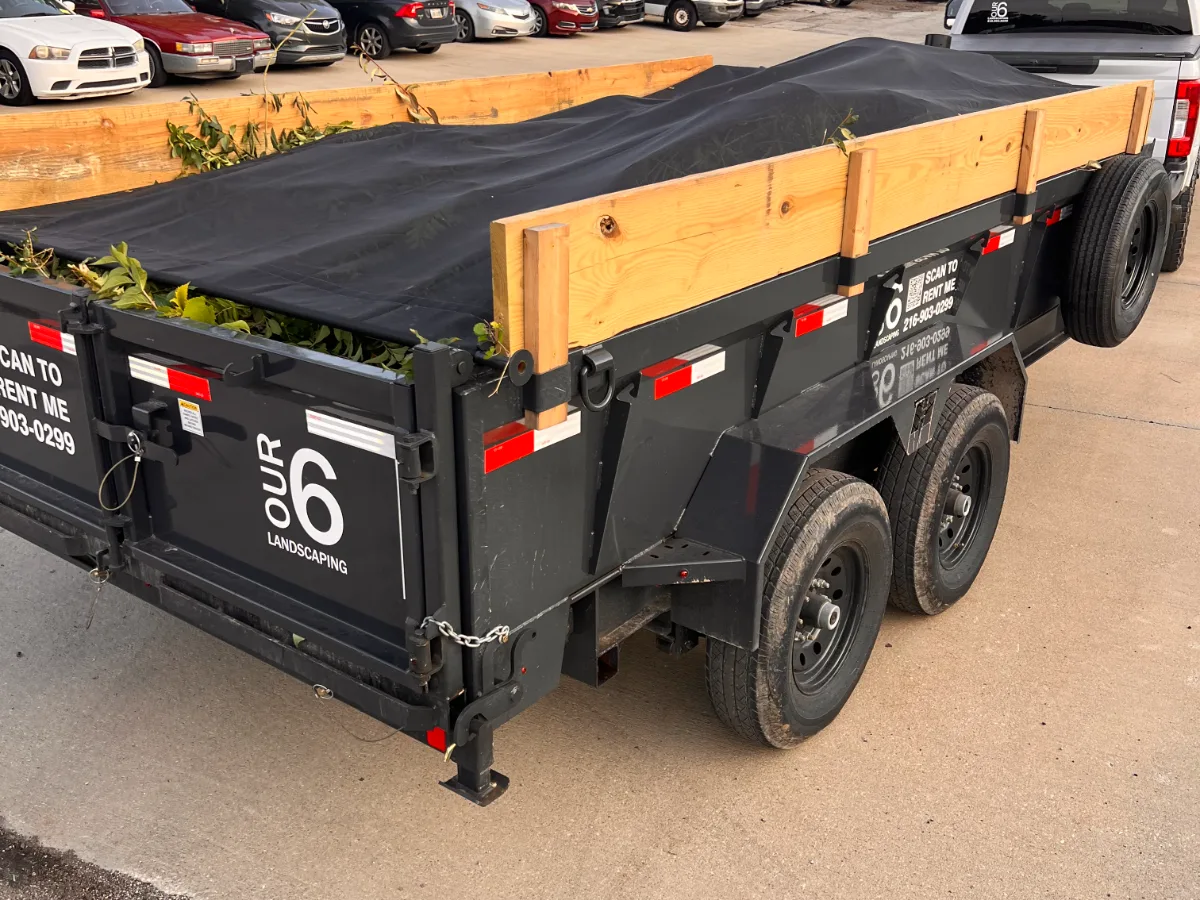 Tarped dump trailer loaded with brush, hooked to our truck